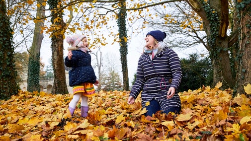 A child and lady wrapped up warm, playing in autumn leaves